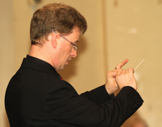 Close up of Andrew, baton in hand, conducting
